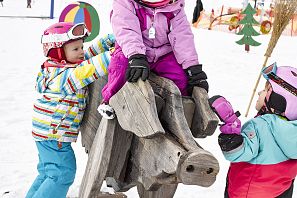 Zona de prácticas de Hexenwiese en el valle de SkiWelt Söll Niño sobre un cerdo de madera en un parque infantil de nieve