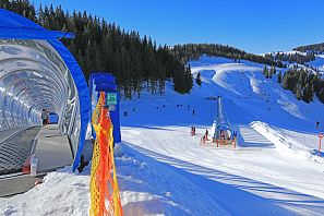 Alfombra mágica con túnel en el paraíso invernal de Ellmi, en la estación de montaña Hartkaiserbahn de SkiWelt Ellmau, con vistas a la montaña y a la pista de prácticas bajo un cielo azul brillante.