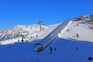 Tovertapijt met tunnel in Ellmi's winterwonderland bij het bergstation van de Hartkaiserbahn in SkiWelt Ellmau met uitzicht op de berg en de oefenpiste onder een stralend blauwe hemel