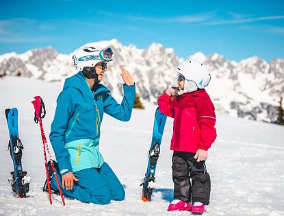 kind-macht-high-five-mit-elternteil-auf-piste-mit-wilder-kaiser-im-hintergrund-4