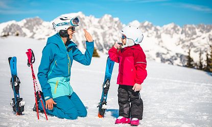 kind-macht-high-five-mit-elternteil-auf-piste-mit-wilder-kaiser-im-hintergrund-5