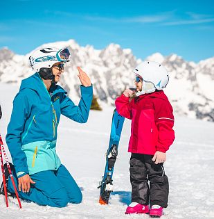 kind-macht-high-five-mit-elternteil-auf-piste-mit-wilder-kaiser-im-hintergrund-8